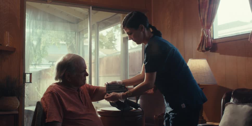 A nurse is taking an elderly mans blood pressure in his living room