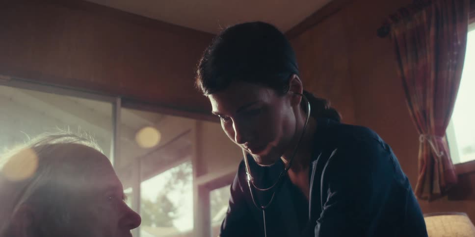 A nurse wearing a stethoscope attends to an elderly man in a home