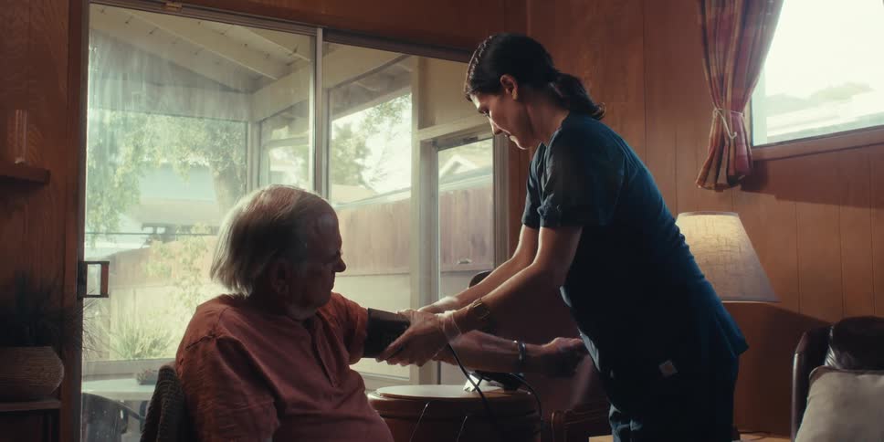 A nurse takes the mans blood pressure at home