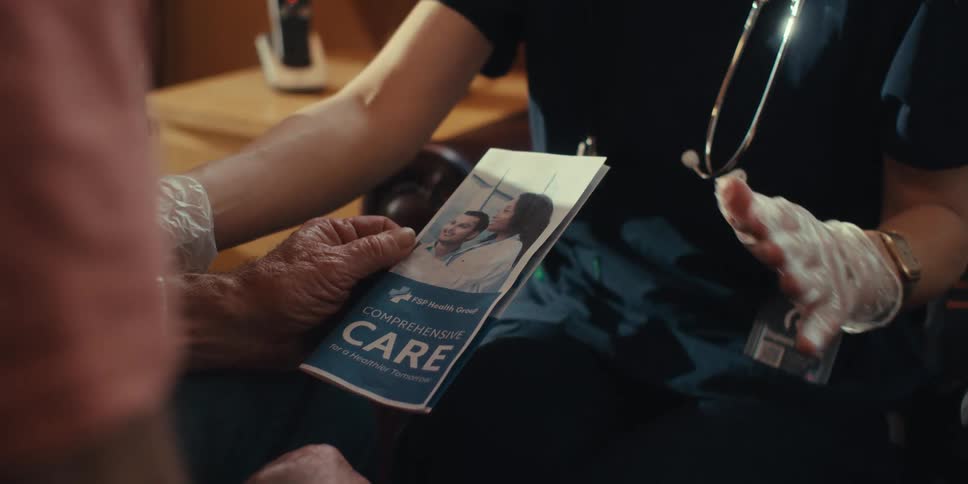 An elderly patient with a pamphlet is talking to a nurse or doctor about some form of treatment