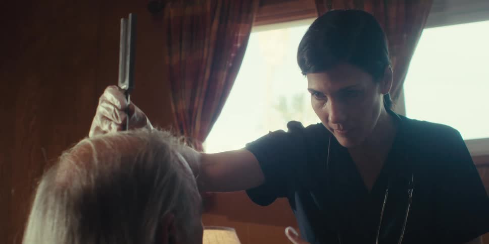 A nurse places a tuning fork over the head of a patient in a home setting