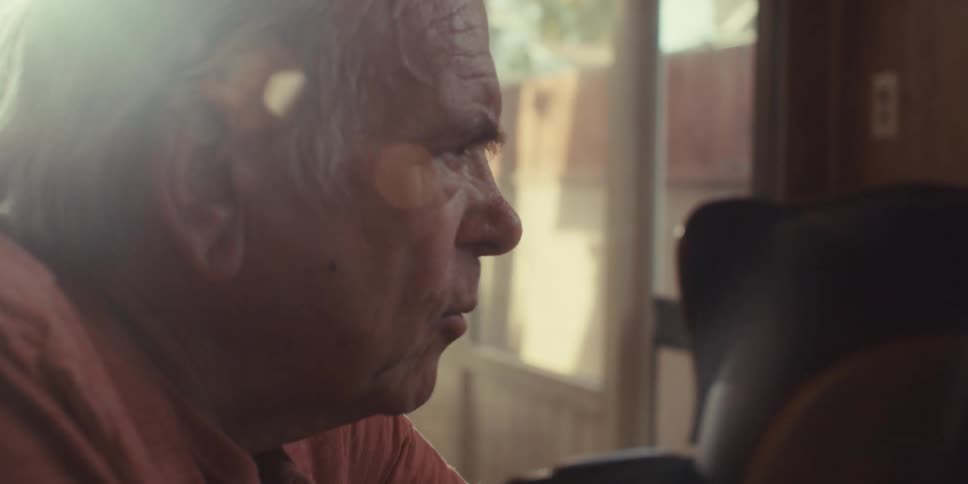 A closeup of an elderly mans face looking sad or confused as he talks to someone at home on a bright day