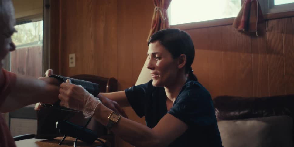 A nurse measures the blood pressure of an elderly man sitting on a couch at home
