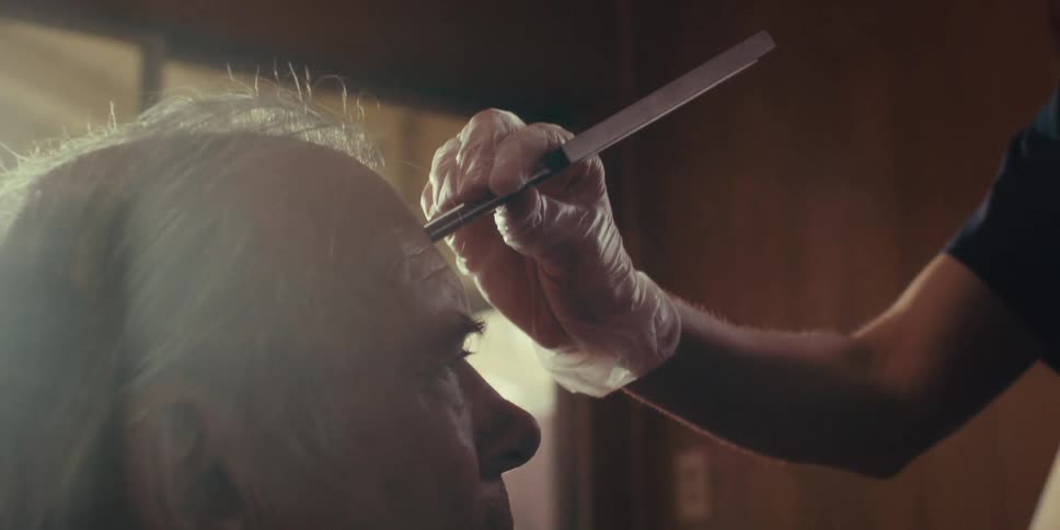 A nurse gently holds an instrument to an elderly patients forehead in a brightly lit room at home