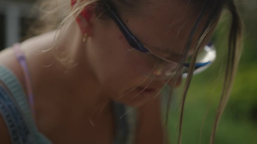A womans head featuring blonde hair and goggles as she works in the garden