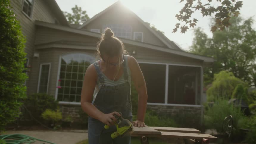 Woman sanding wood with a sander outside in her backyard