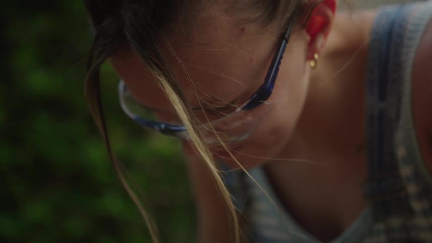 A woman with light colored hair and goggles looks down as she gardens