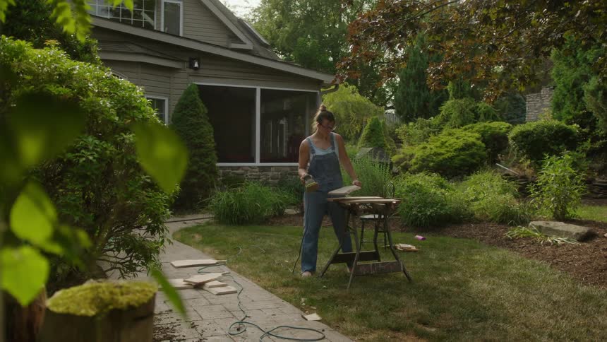 A woman is sanding wood in the yard
