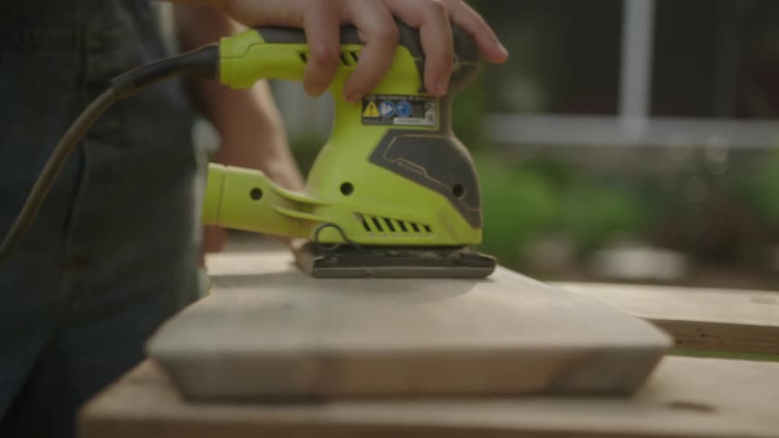 A mans hand smooths down some wooden planks with an electronic sanding tool