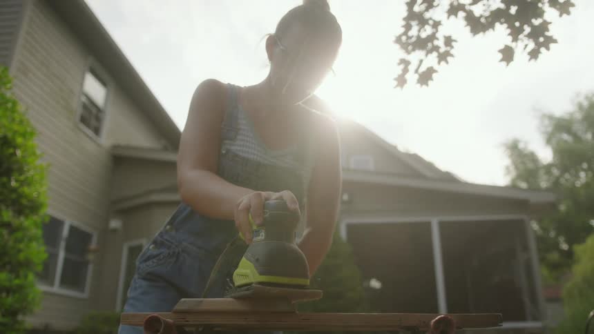 Woman sanding piece of wood in her yard with an electrical sander