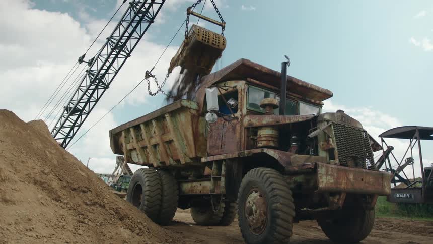 A crane dumps dirt into a truck