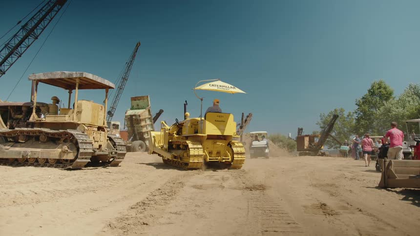 Bulldozers and cranes operate at a construction site while several people observe the activity