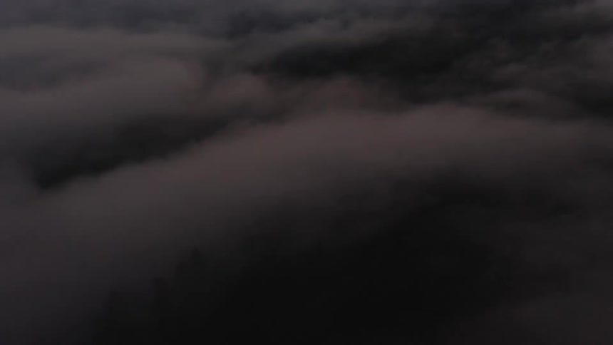 An aerial perspective moves steadily forward above a thick blanket of dark clouds in low light revealing subtle shifts in the atmospheric texture