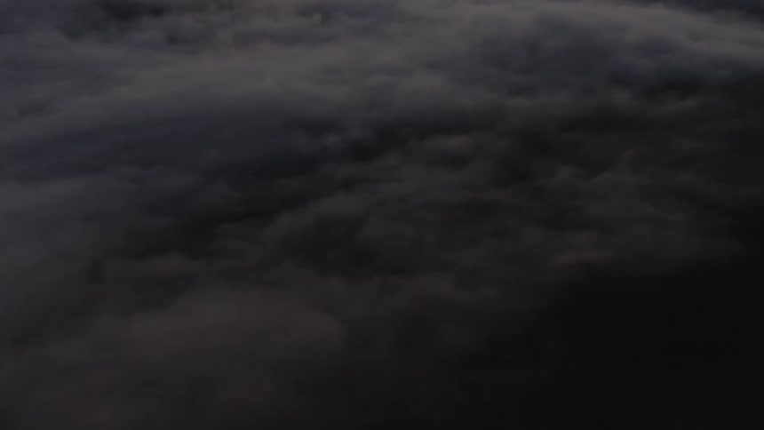 An aerial shot glides forward and slightly downward over thick dark clouds in a dimly lit sky