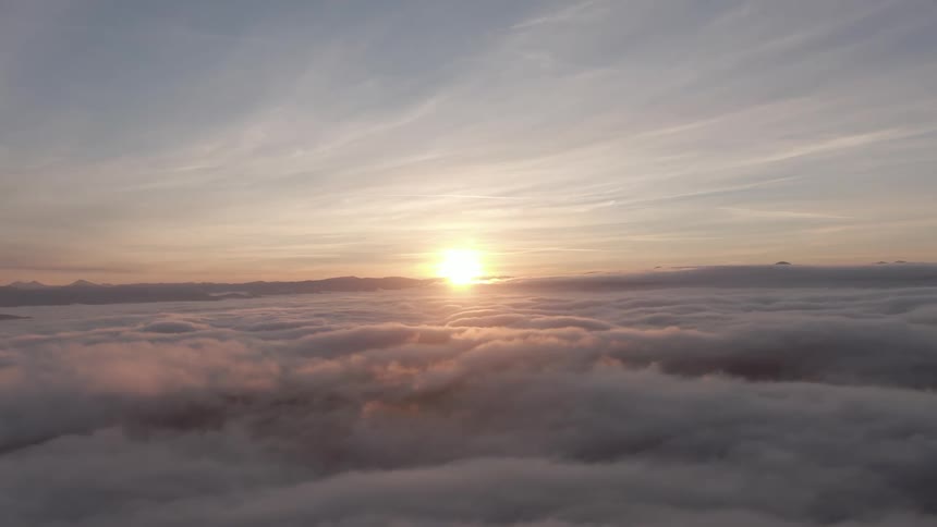 The sun setting above a thick blanket of clouds casting a warm golden light across the undulating cloudscape and the horizon