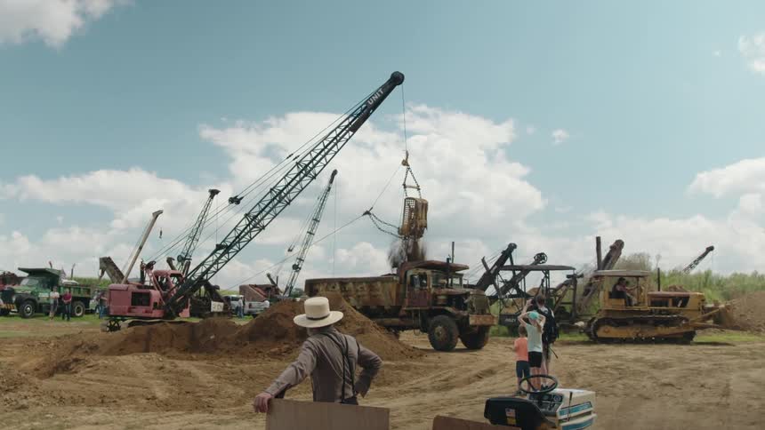 People watch the excavator lift dirt into a dump truck