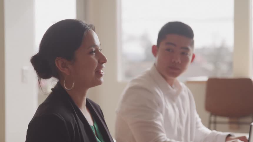 Two people engage in a conversation in a welllit office with large windows letting in natural sunlight