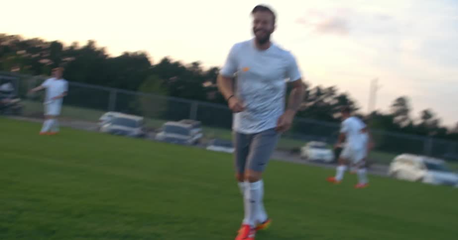 Men play soccer on a grassy field at sunset