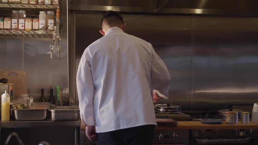 The back of a man in white chef attire cooking in a modern restaurant