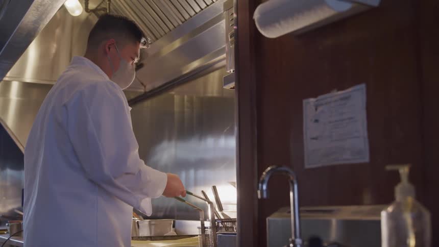 A chef is shaking a fry basket over a fryer