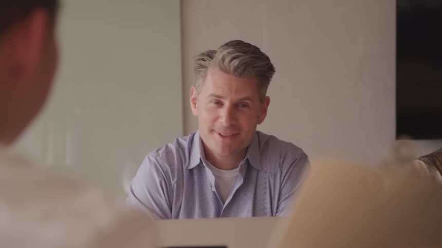 People seated in an office talk to a person holding a clipboard in a brightly lit room