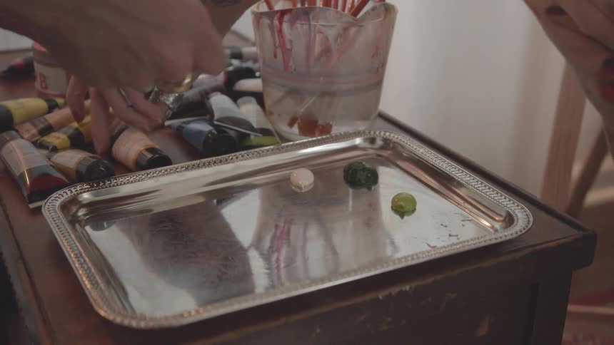 The hands of two people each pick up tubes of paint and squirt them onto a tray