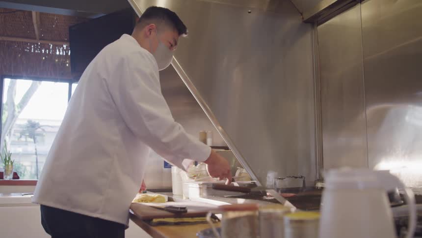Male chef wearing a face mask flips meat while cooking in the kitchen