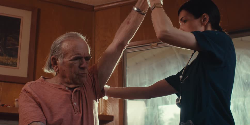 Female medical professional manipulates the arm of an elderly man during a home healthcare visit