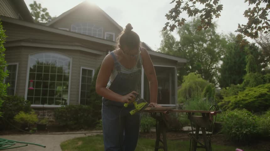 A woman is sanding wood on a sunny day