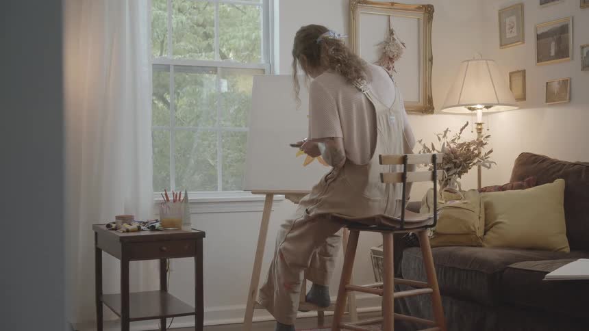 Female painter sitting on a stool in her living room paints