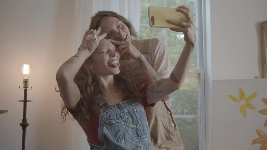 Women who are twins take a picture with a cellphone