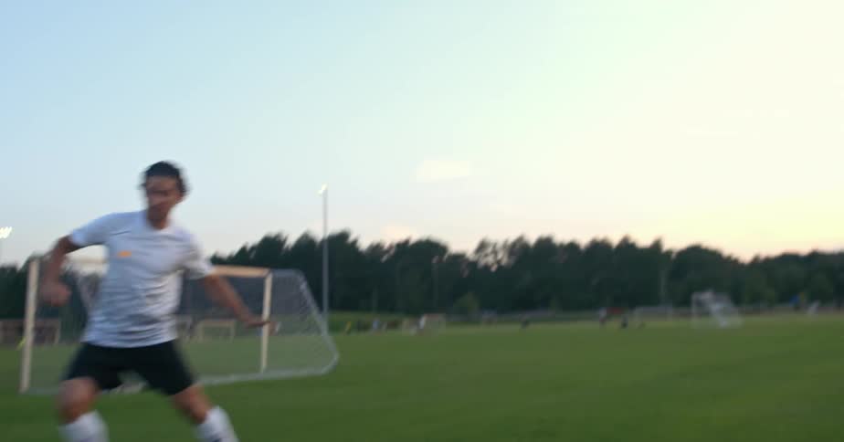 A soccer player is passing and receiving the ball on a field at dusk