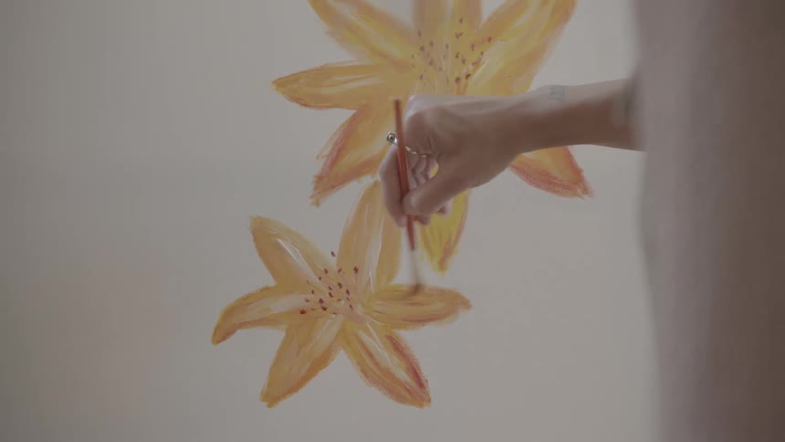 A closeup of a womans hands delicately painting flowers with oil on a canvas in a welllit room