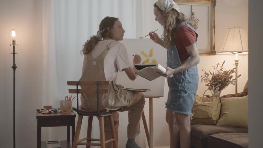 Two women are painting on a canvas in a cozy room