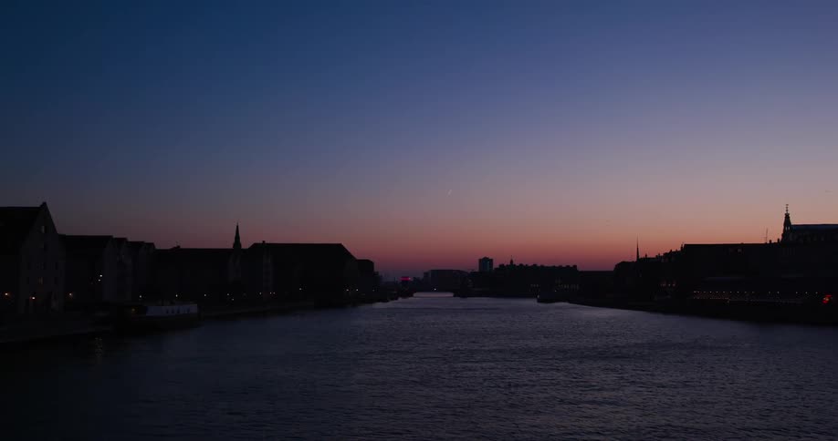 River passes between residential buildings while a red afterglow tints the horizon