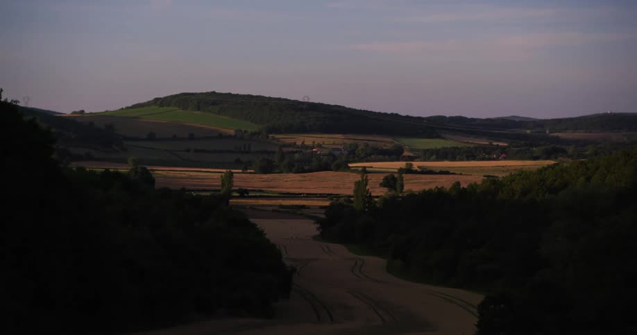 Rolling hills with alternating patches of lush greenery and golden fields stretch under a crisp clear sky