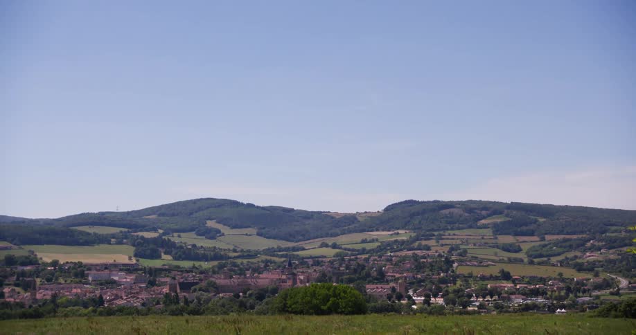 A sprawling town nestled in a valley surrounded by rolling green hills and patches of farmland under a clear pale blue sky