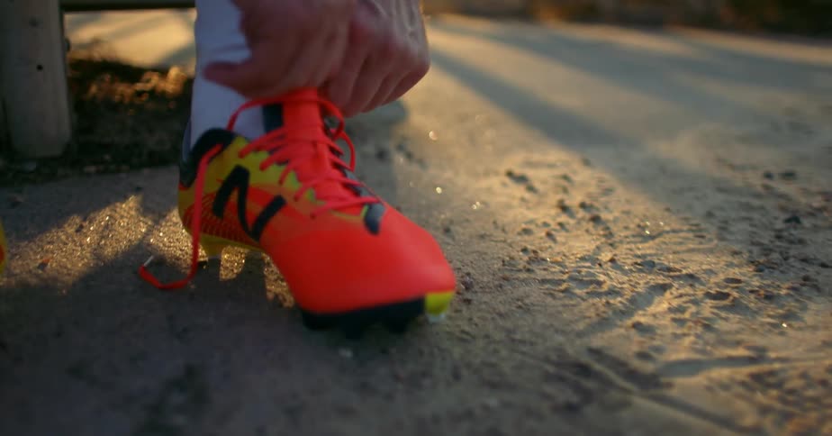 A man sits on a bench and puts on his cleats