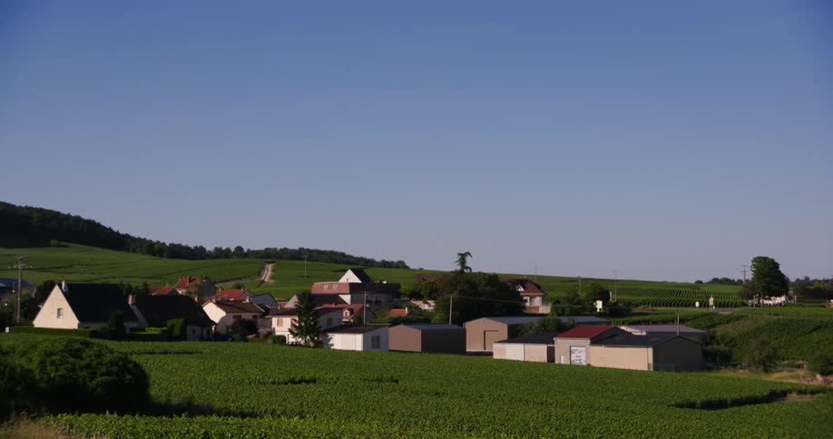 A quaint village nestled among rolling green vineyards under a clear bright blue sky