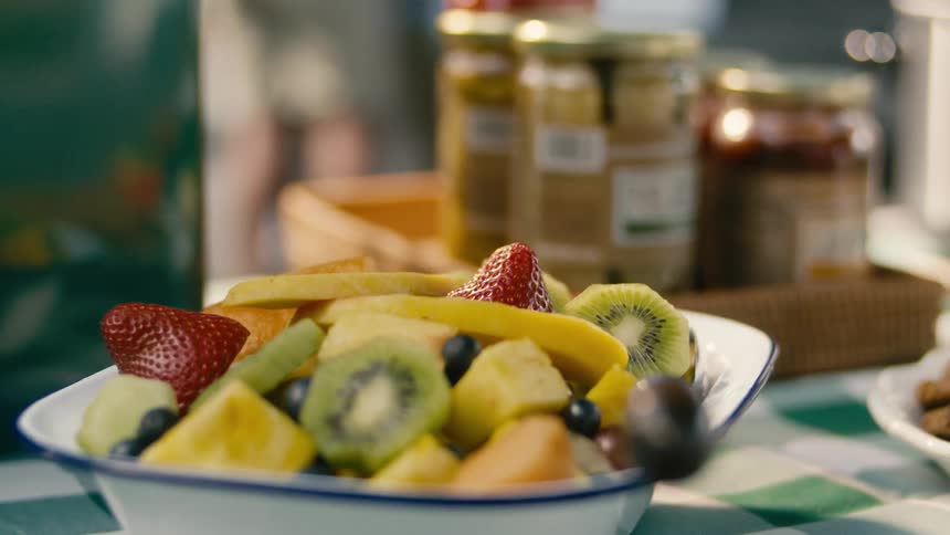 Bowl of fresh fruit displayed on checkered tablecloth next to glass jars