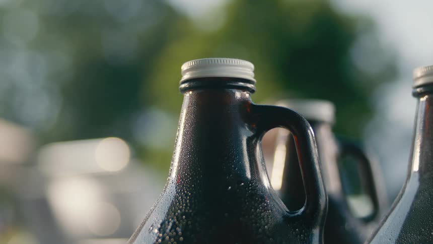 Three large glass jugs sweat while standing outdoors during the daytime