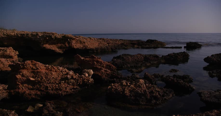 A rocky shoreline meeting a calm dark sea under a dusky sky likely at twilight