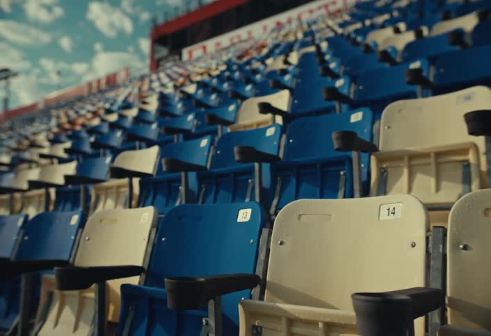 Rows of empty blue and beige stadium seats under a partly cloudy sky