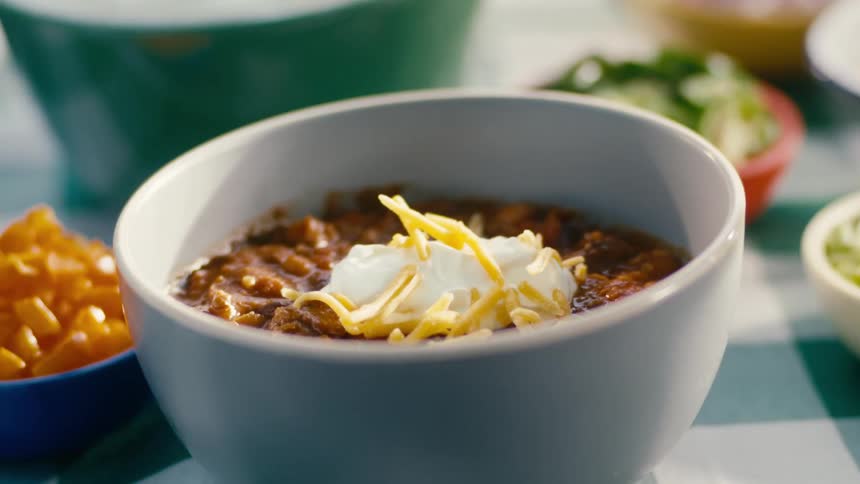 Adding cheese over sour cream to a bowl of chili