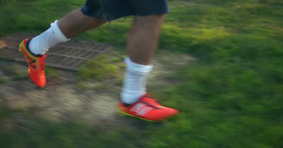 Man wearing brightly colored orange shoes walking across a grassy field
