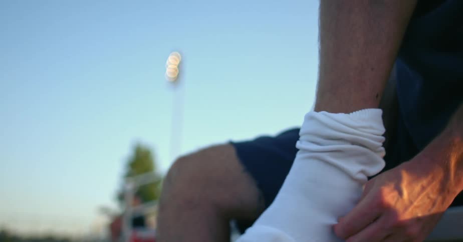 A person putting socks on while sitting on a bench outside