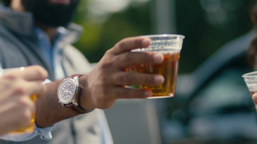 Three men are talking and holding glasses of beer and then they toast and start drinking