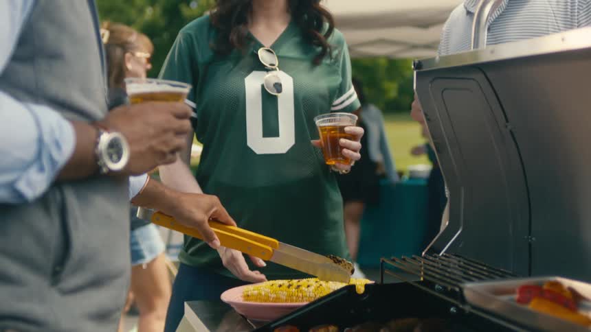 A man serves grilled corn to friends at an elegant barbecue on a sunny day