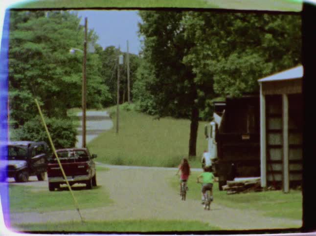 Vintage footage of a young girl and boy riding their bicycles down a lane