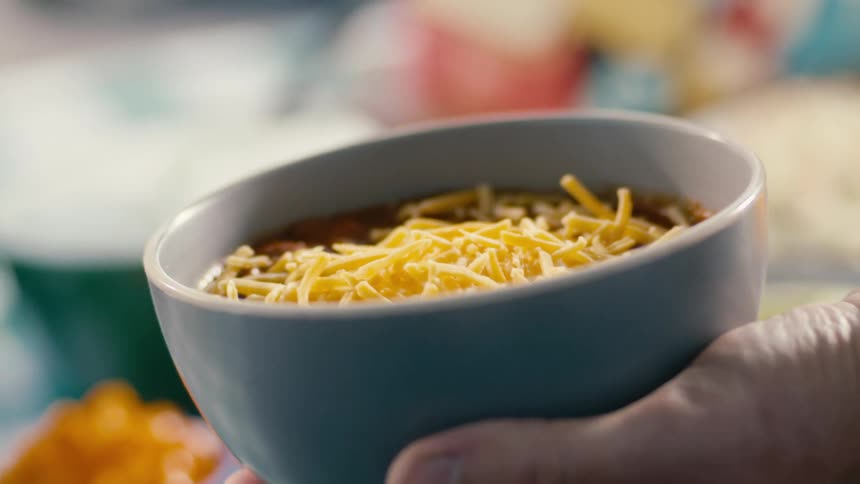 A person is putting ingredients on their bowl of chili